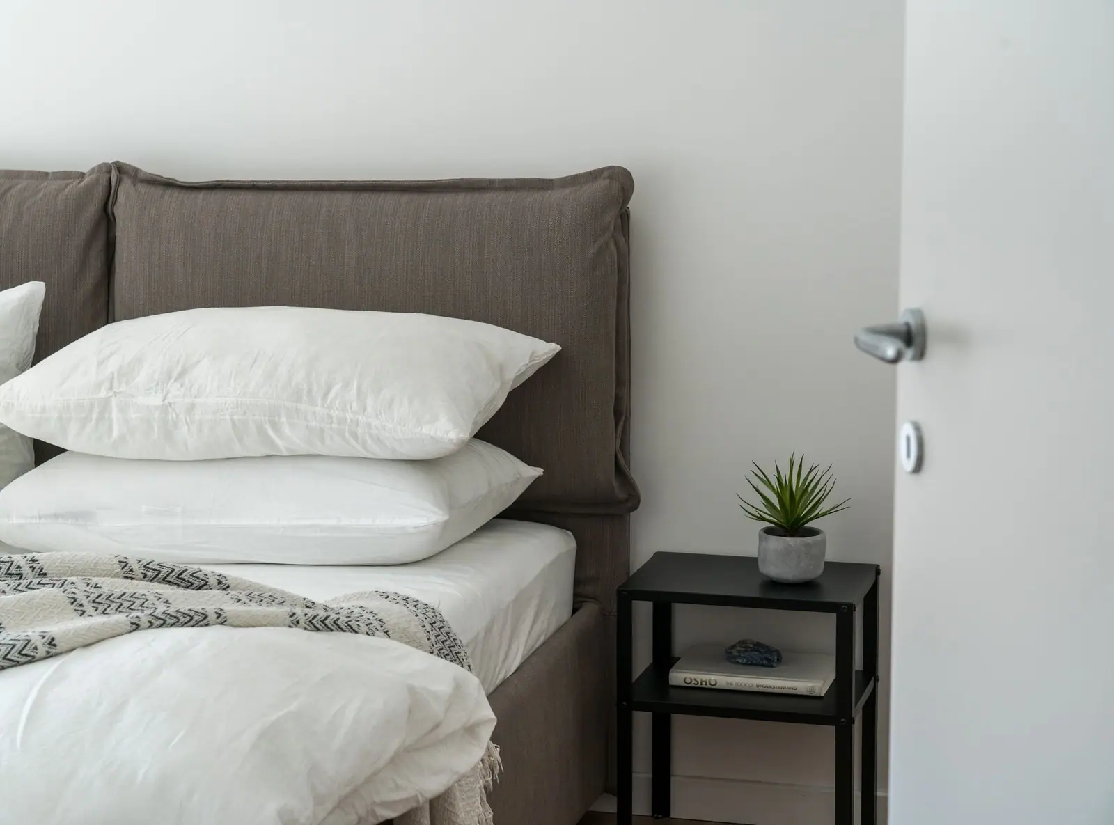Bright bedroom with white pillows on a made bed and a bedside table with a plant