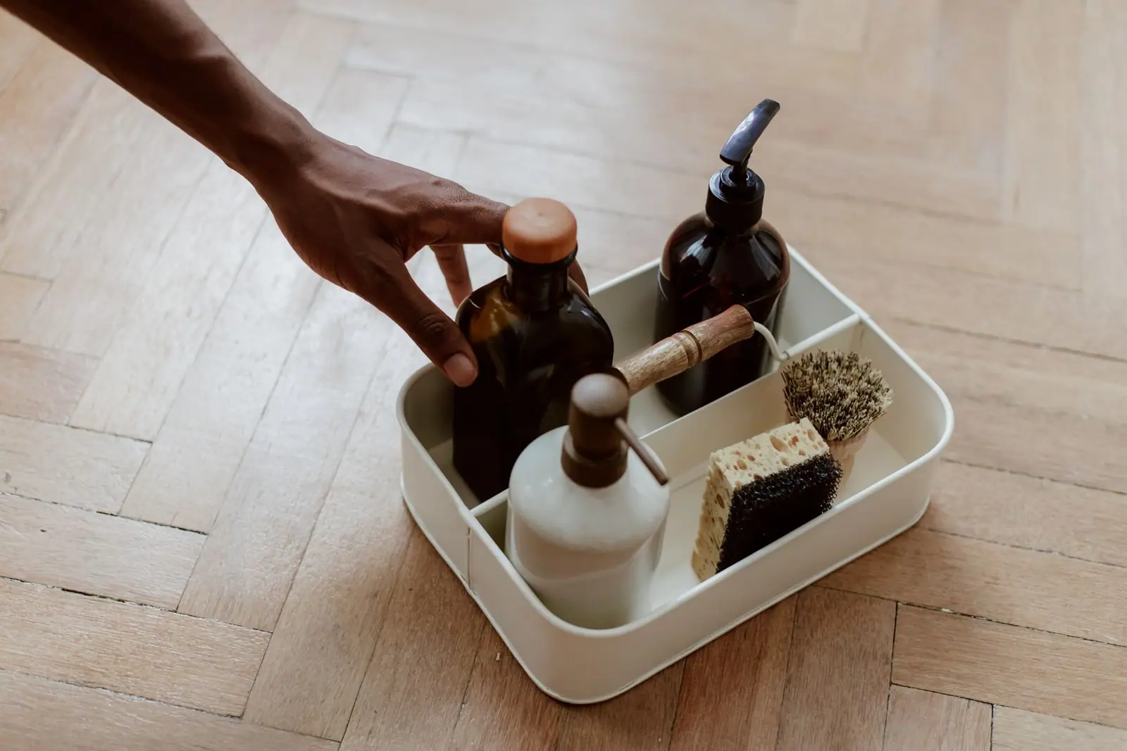 Hand setting down a caddy of cleaning bottles and brushes on a wooden floor
