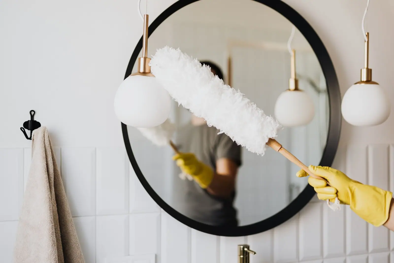 Gloved hand dusting a round mirror with a feather duster