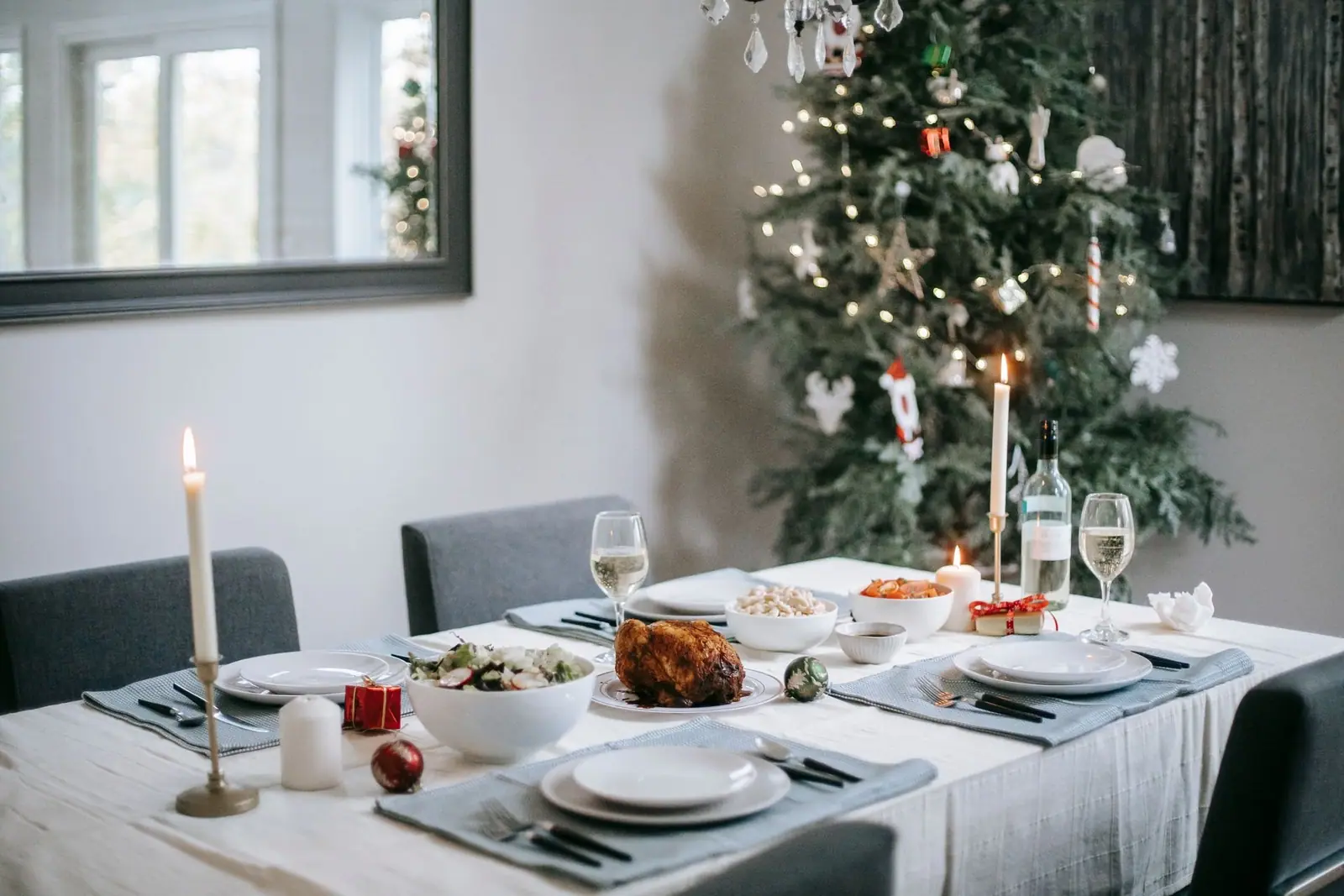 Dining table set for a holiday dinner with a decorated tree behind it