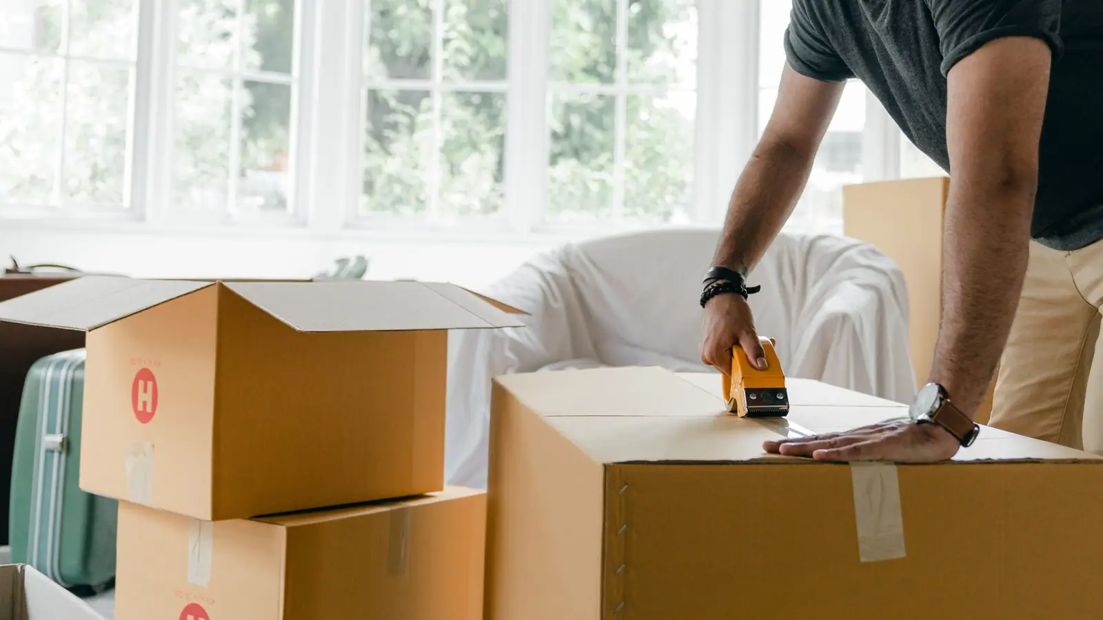 Hands taping a moving box shut in a sunny room