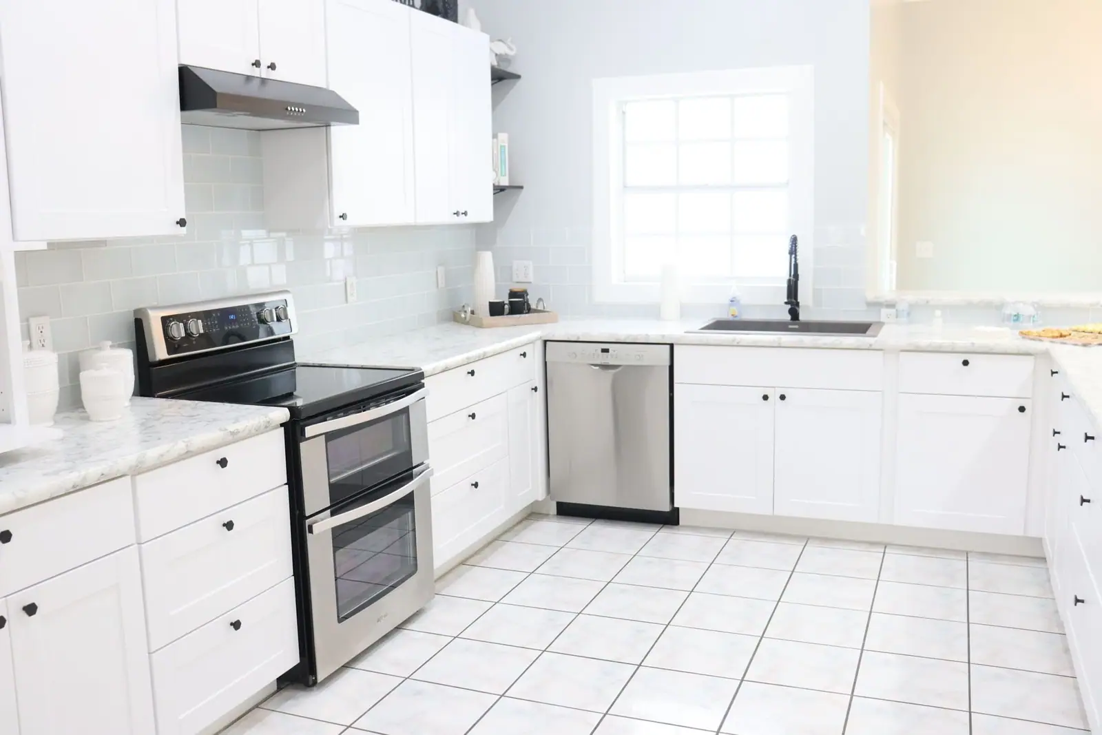 Bright white kitchen with stainless appliances and a tiled floor