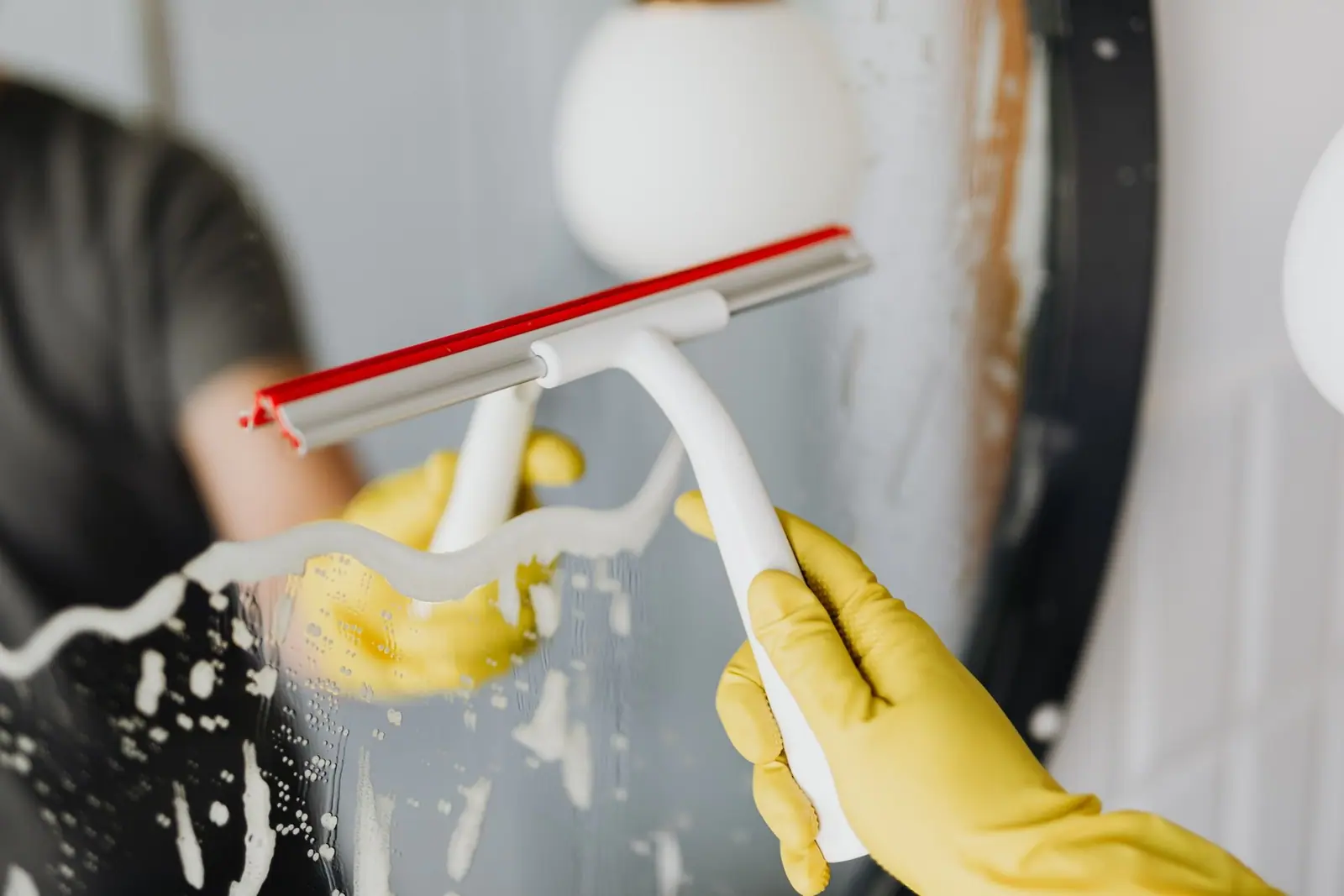Gloved hand drawing a squeegee across soapy glass