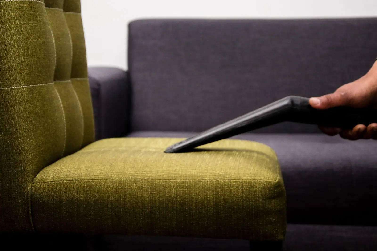 Vacuum nozzle cleaning the seat of a green fabric armchair